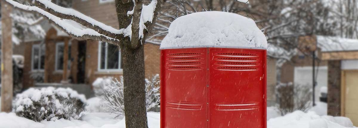 Brick red porta potty rental toilet covered with snow - renting a porta potty in the winter